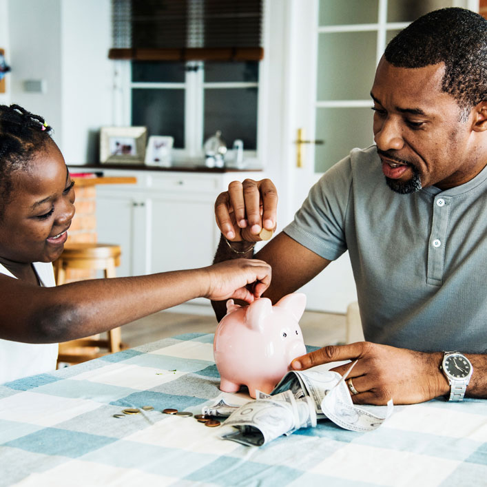 Un hombre y una niña sentados en una mesa con una alcancía, ahorrando juntos para su futuro.
